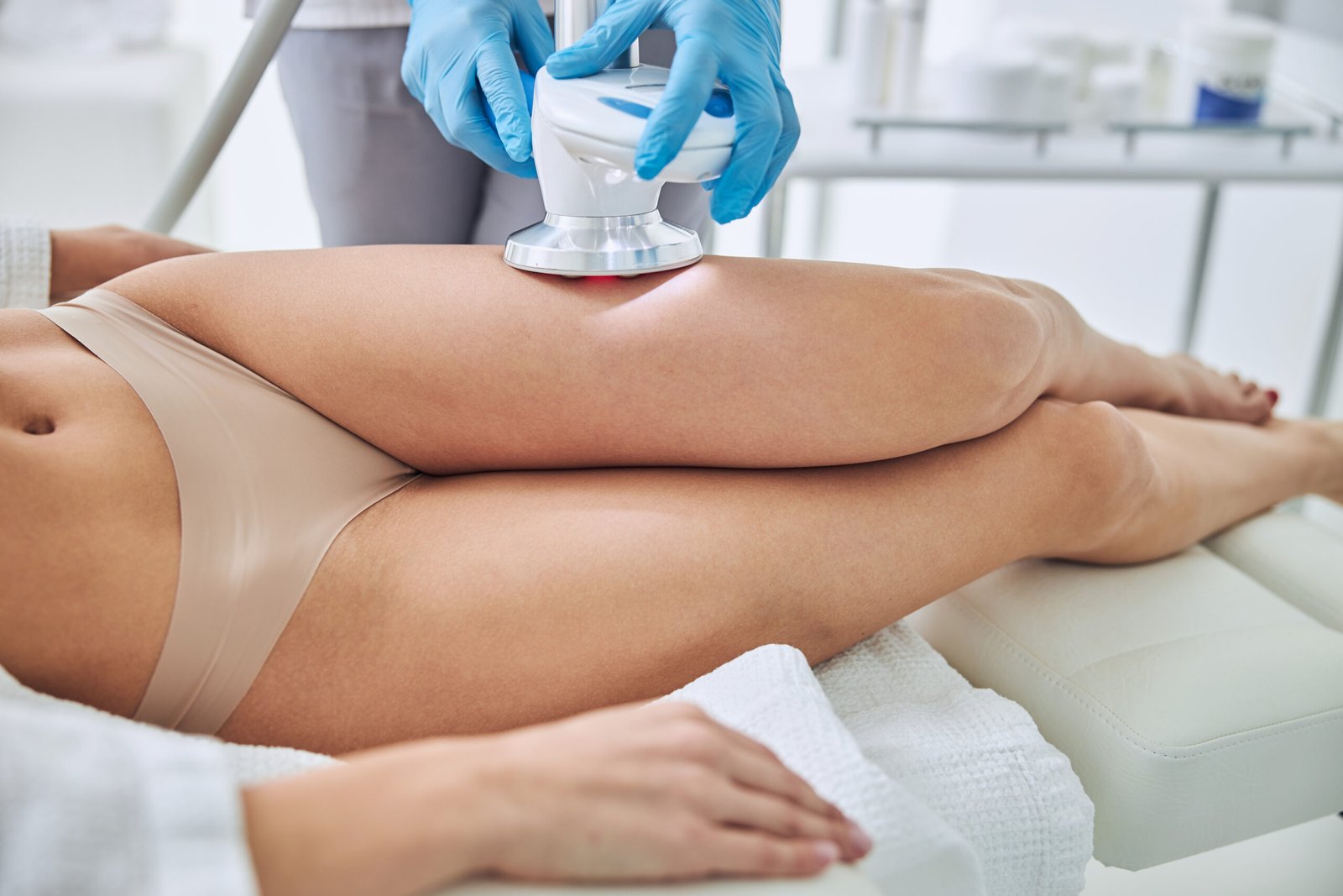Cropped head portrait of unrecognized female patient lying on medicine chair while receiving ultrasound cavitation body contouring treatment in beauty clinic